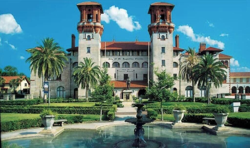 A large, historic building with two towers, a central courtyard, and a fountain.