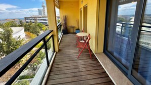 A balcony with a wooden floor, a small table with chairs, and a potted plant. - Tejo Balcony Expo (Lisbon)