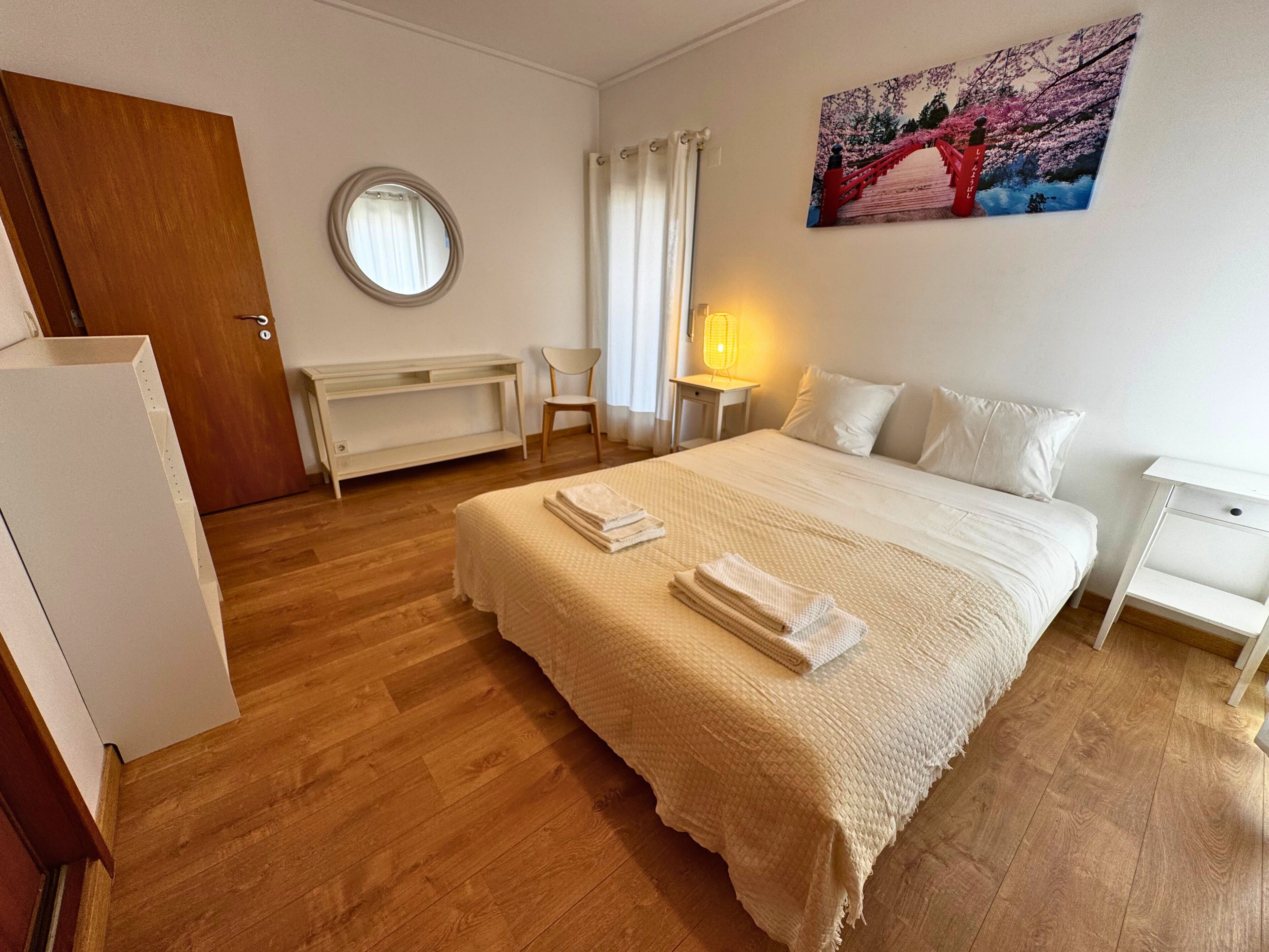A hotel room with a bed, a chair, a desk, a lamp, and a painting on the wall.
