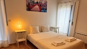 A neatly arranged bedroom with a bed, bedside table, lamp, and a painting of a cherry blossom bridge. - Tejo Balcony Expo (Lisbon)