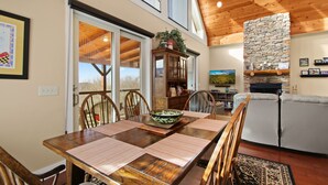A dining area with a wooden table, chairs, and a view through glass doors. - Cabin with Long Range Views, Hot Tub, Game Room (Beech Mountain)