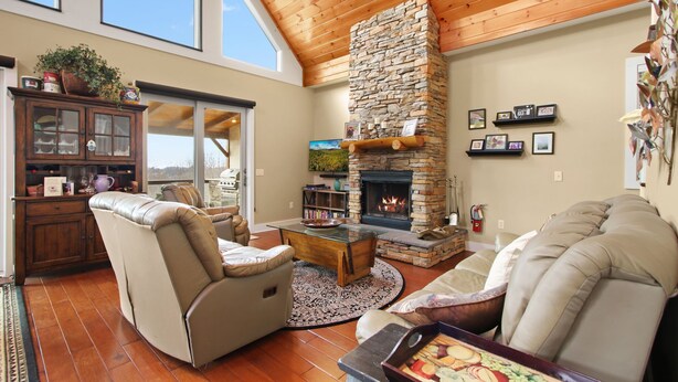 A cozy living room with a stone fireplace, leather sofas, and a wooden ceiling. - Cabin with Long Range Views, Hot Tub, Game Room (Beech Mountain)
