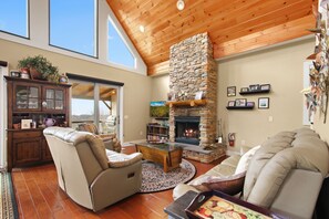 A cozy living room with a stone fireplace, leather sofas, and a wooden ceiling. - Cabin with Long Range Views, Hot Tub, Game Room (Beech Mountain)