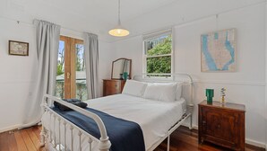 A bedroom with a bed, a nightstand, a map on the wall, and a window with curtains. - Blackheath Breeze Cottage - Nature Escape (Blackheath)