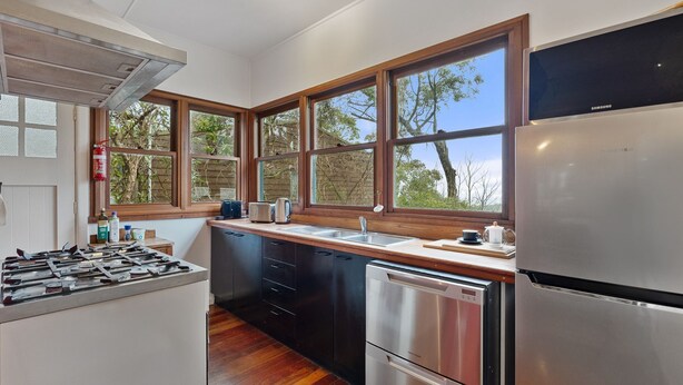A modern kitchen with a stainless steel refrigerator, a dishwasher, a stove, and a sink. There are large windows providing natural light and views of trees. - Blackheath Breeze Cottage - Nature Escape (Blackheath)