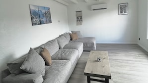 Un saló modern amb un sofà seccional gris, una taula baixa de fusta i un finestral gran.