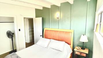 Een slaapkamer met een bed, nachtkastje, lamp en een ventilator.