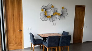 Een moderne eetruimte met een houten tafel en vier stoelen, een decoratief wandobject en twee houten deuren.