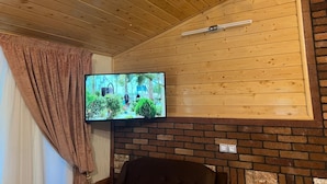 A room with a television mounted on a brick wall, wooden ceiling, and a brown curtain. - Villa De Anna (St.-Rémy-de-Provence)