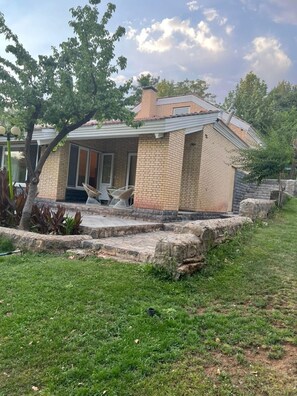 A single-story brick house with a covered porch, a stone retaining wall, and a grassy yard. - Villa De Anna (St.-Rémy-de-Provence)