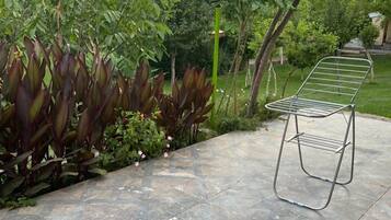 Un patio con una silla de metal, baldosas de piedra y abundante vegetación.