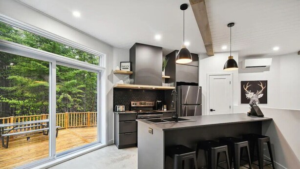 A modern kitchen with a large island, bar stools, and a view of a wooden deck.