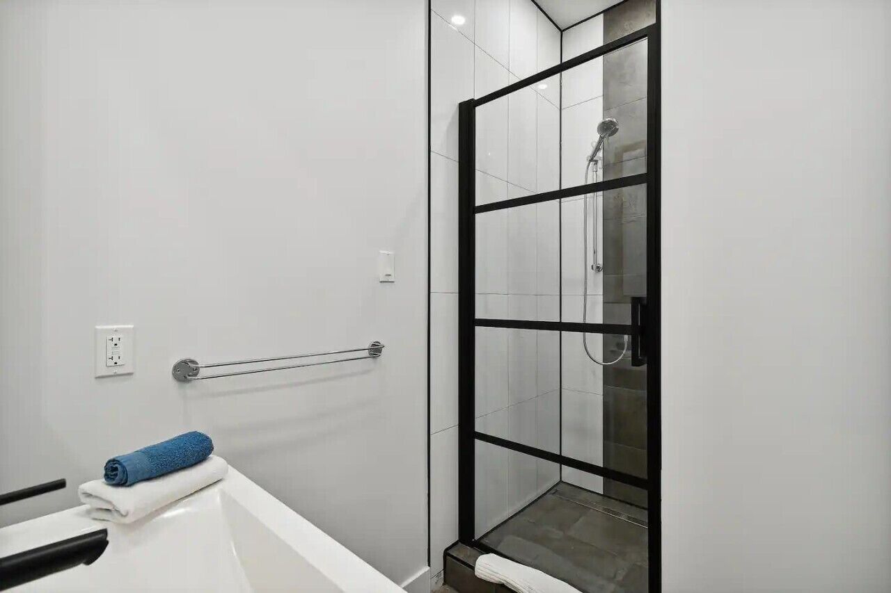 Un baño moderno con ducha de vidrio, bañera blanca y toallero con una toalla azul.