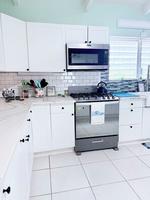 A modern kitchen with white cabinetry, a built-in microwave, a gas stove, and a stainless steel range hood.