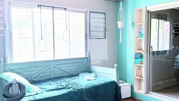 Une chambre avec un lit, une fenêtre, une suspension en macramé et une porte donnant sur un balcon.