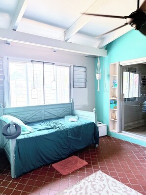 A bedroom with a bed, a window, a hanging macrame light, and a door leading to a balcony.