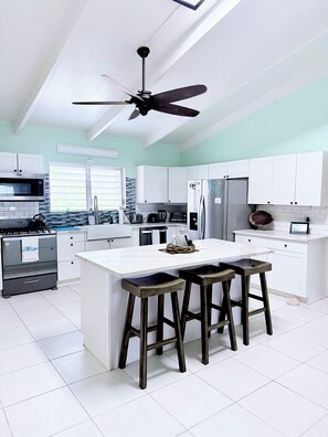 A modern kitchen with white cabinetry, a central island with stools, a ceiling fan, and a stainless steel refrigerator.