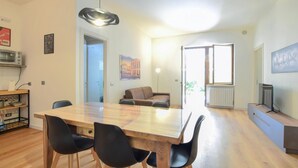 Un espace de vie moderne comprenant un coin repas, un canapé, un téléviseur et un tableau représentant le Colisée.