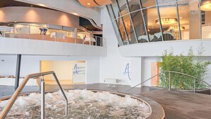 Un espace piscine intérieur moderne doté d’un toit en verre, d’un jacuzzi et d’une plante en bambou.