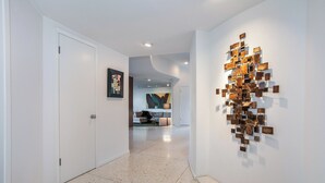 A hallway with a modern art installation on the right wall, a door on the left, and a living area in the background. - Luxe Hollywood Hills Modern, City Views, 84°F Pool (Los Angeles)