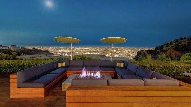 A deck with a fire pit, two umbrellas, and a sofa facing a cityscape at night. - Luxe Hollywood Hills Modern, City Views, 84°F Pool (Los Angeles)