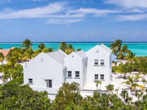 Um edifício branco com telhado plano, rodeado por palmeiras e uma praia.