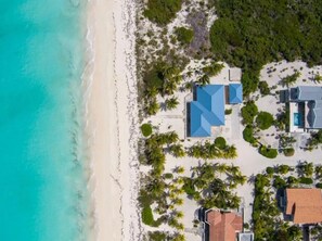 An aerial view of a beachfront property with a swimming pool, multiple buildings, and lush greenery. - Now avail! 3-bdrm House with pool in tranquil Whitby Haven w/beach & ocean views (Whitby)