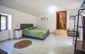 Ein Schlafzimmer mit Bett, Nachttisch, Lampe und Blick ins Freie durch ein Fenster.