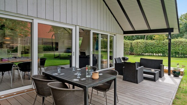 An outdoor patio with a table and chairs, large sliding glass doors, and a view of a garden. - 3 bedroom amazing home in Lundby (Lundby)