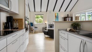 A modern kitchen with white cabinets, a built-in oven, and a coffee maker. There is a window with a view of greenery outside. - 3 bedroom amazing home in Lundby (Lundby)