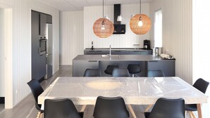 Une cuisine moderne dotée d’un îlot central, de chaises noires et de deux suspensions en osier.