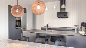 Une cuisine moderne dotée d’un îlot central, d’appareils électroménagers en acier inoxydable et de luminaires suspendus.