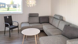 Un salon moderne avec un canapé d’angle, une table basse ronde blanche et un fauteuil en osier.