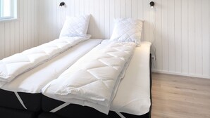 Un lit avec une couette et des oreillers blancs à motifs matelassés, une tête de lit noire et un plancher en bois.