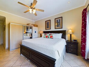 Une chambre à coucher comprenant un lit, un ventilateur de plafond, une table de chevet avec une lampe et une armoire.