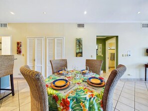 Un coin repas avec une table ronde, six chaises en osier et une nappe à motifs floraux.