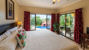 Une chambre spacieuse dotée d’un grand lit, d’un ventilateur de plafond et offrant une vue sur une piscine et un espace de détente extérieur.