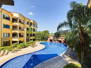 Un complexe hôtelier doté d’une grande piscine, de chaises longues et d’un immeuble à plusieurs étages avec des balcons.