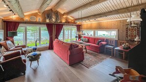 A cozy living room with a red sofa, wooden flooring, and a large window overlooking greenery.