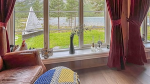 A cozy room with a view of a green landscape through large windows, a leather sofa, and a window sill with decorative items.