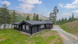 A log cabin with a steeply pitched roof, a small porch, and a gravel driveway leading to the entrance.