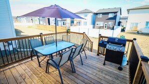 A wooden deck with a table and chairs, a barbecue grill, and a large umbrella. - New Modern & Luxury 3BR+2.5 Bath w/Garage Home in Saskatoon, SK (Saskatoon)