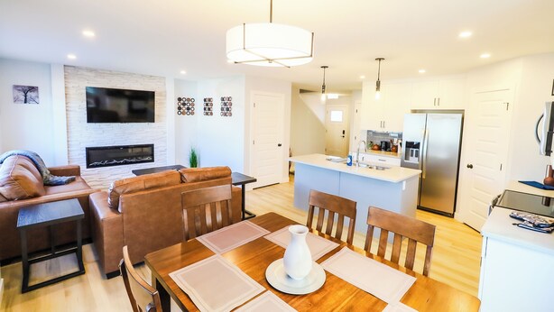 A modern living room with a sofa, dining table, and kitchen area. - New Modern & Luxury 3BR+2.5 Bath w/Garage Home in Saskatoon, SK (Saskatoon)