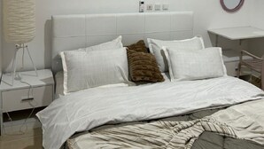 A modern bedroom with a neatly made bed, a bedside table, a lamp, and a small desk with a chair.
