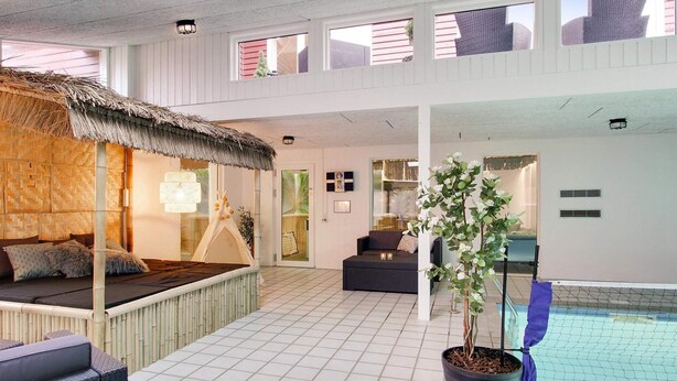 A spacious indoor area with a thatched-roof seating area, a potted plant, and a pool. - 5 Star Holiday Home in Ebeltoft (Ebeltoft)