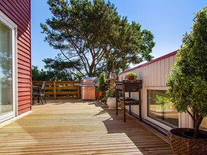 A wooden deck with a barbecue grill, a dining table with chairs, and a potted tree. - 5 Star Holiday Home in Ebeltoft (Ebeltoft)