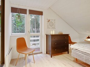 A bedroom with a wooden dresser, a chair, a bed, and a window with a view of trees. - 5 Star Holiday Home in Ebeltoft (Ebeltoft)