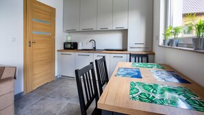 Eine kleine Küche mit weißen Schränken, einer Holztür und einem Essbereich mit Tisch und Stühlen.
