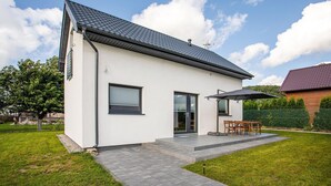 Ein modernes eingeschossiges Haus mit flachem Dach, einer Terrasse und Gartenmöbeln sowie einem gepflegten Rasen.