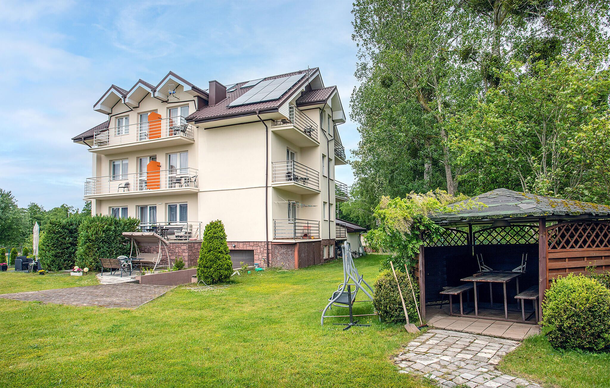 A multi-story residential building with balconies, a covered outdoor seating area, and a well-maintained lawn.